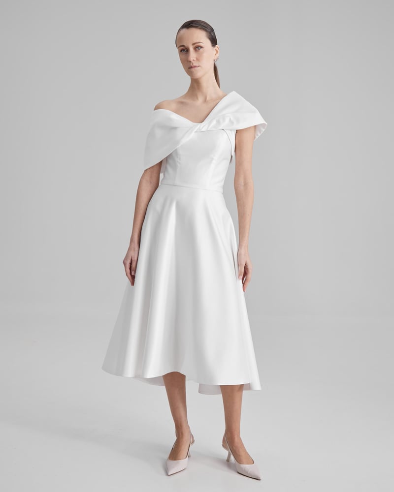 a model wears a white A-line midi wedding dress with oversized detachable asymmetric bow neckline.