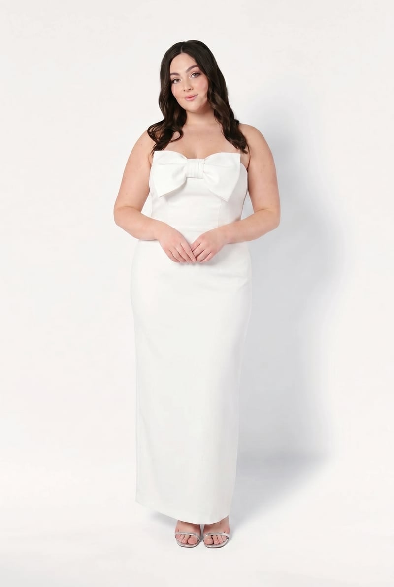 a model wears a strapless pencil style wedding dress with bow detail on the neckline.