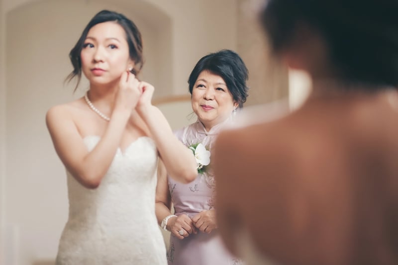 A bride adjusting her earrings as her mother looks on