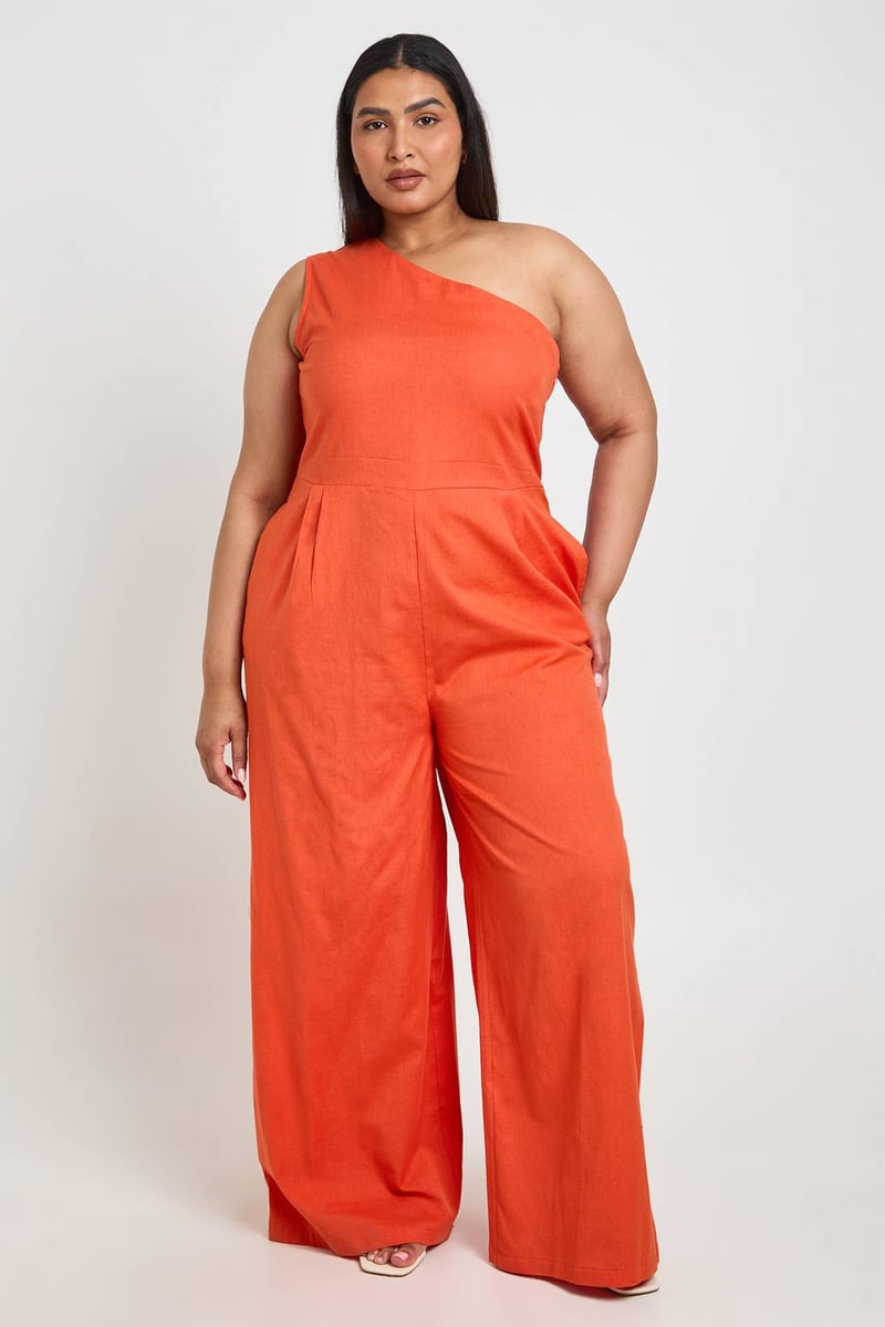 a curve model wears a one-shoulder jumpsuit in burnt orange with wide leg trousers.