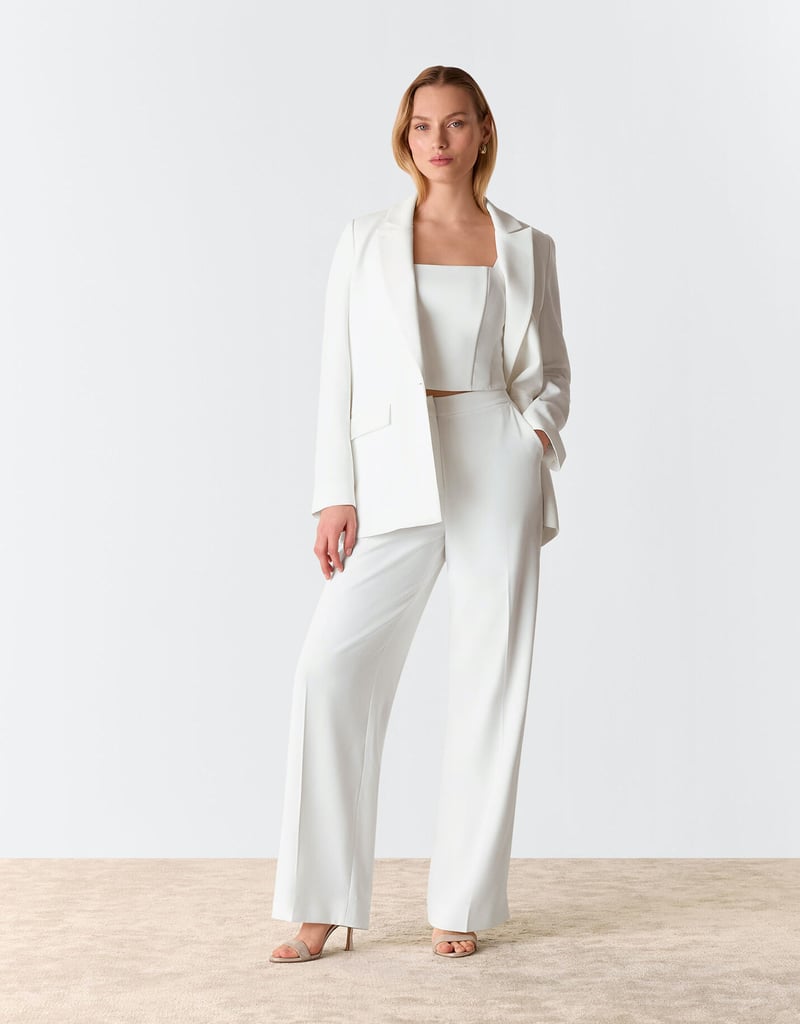 a model wears an ivory bridal suit with wide straight-leg trousers and bandeau top underneath a relaxed blazer.