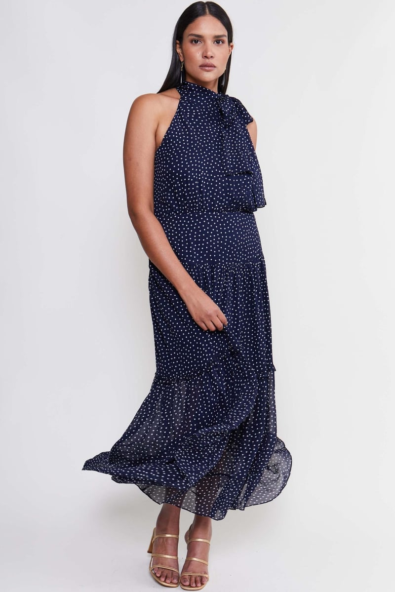a curve model wears a navy blue midi dress with ruffled skirt detail, neck tie and polka dot print.