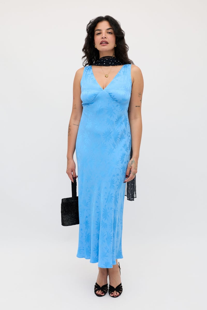a curve model wears a light blue satin jacquard print midi slip dress with black scarf and accessories