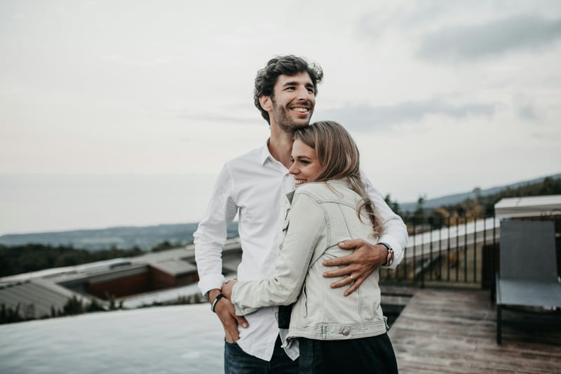 man and woman embracing on a rooftop outside, smiling and hugging