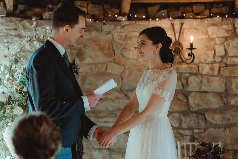 a bride and groom hold hands in their ceremony as the groom reads his wedding vows.
