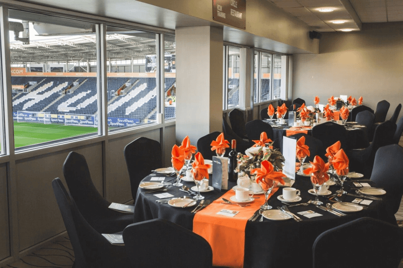 A wedding reception room at MKM Stadium, Hull, with black and orange table settings and views over the football pitch
