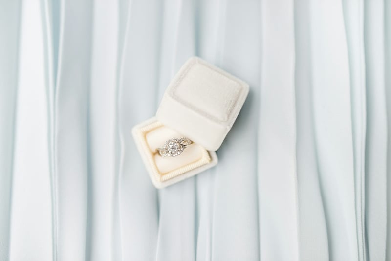 Engagement ring in a white ring box on a pale blue backdrop