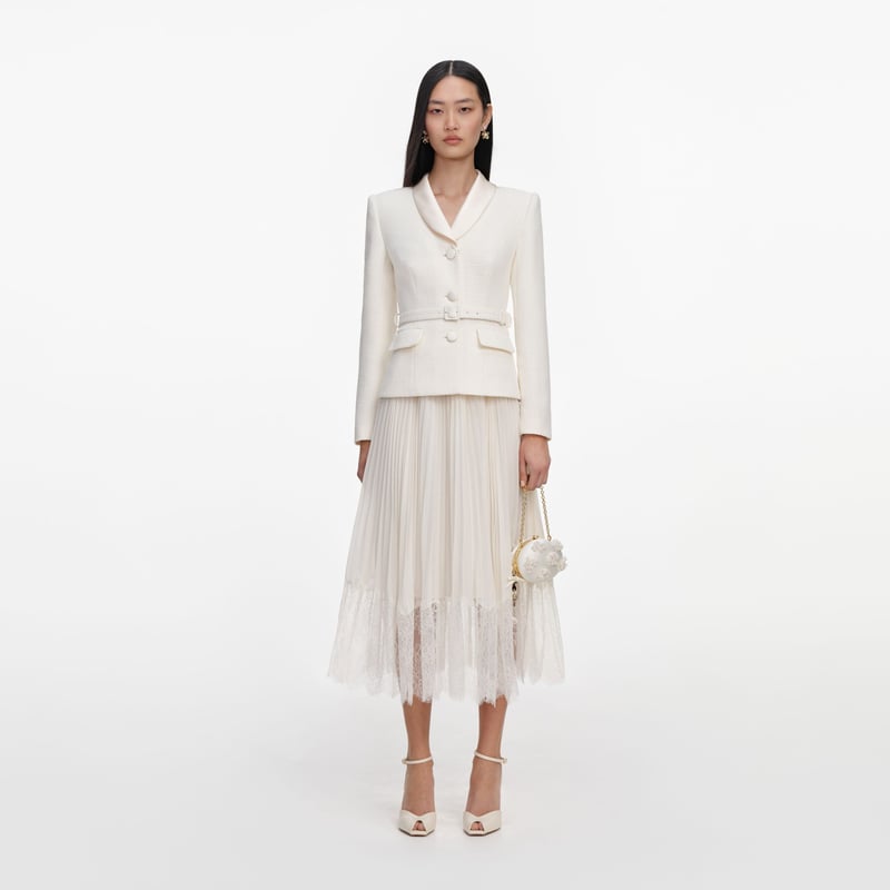 a model wears a white midi dress that looks like a two-piece skirt suit with lace trim skirt and collared jacket with button-down front.