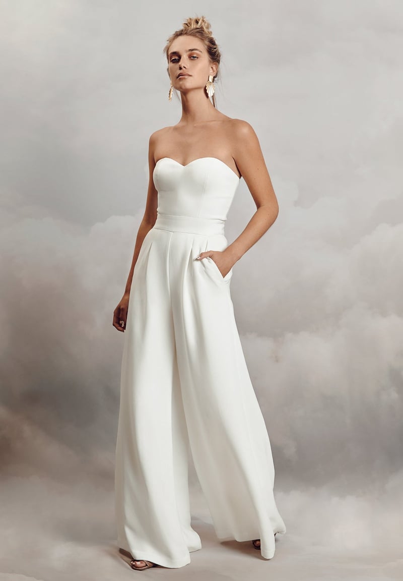 a model wears a strapless white crepe jumpsuit with sweetheart neckline and wide leg trousers.