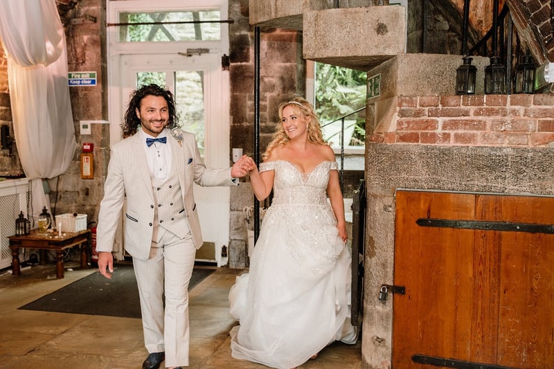 a bride and groom walk hand in hand into their wedding reception, smiling.