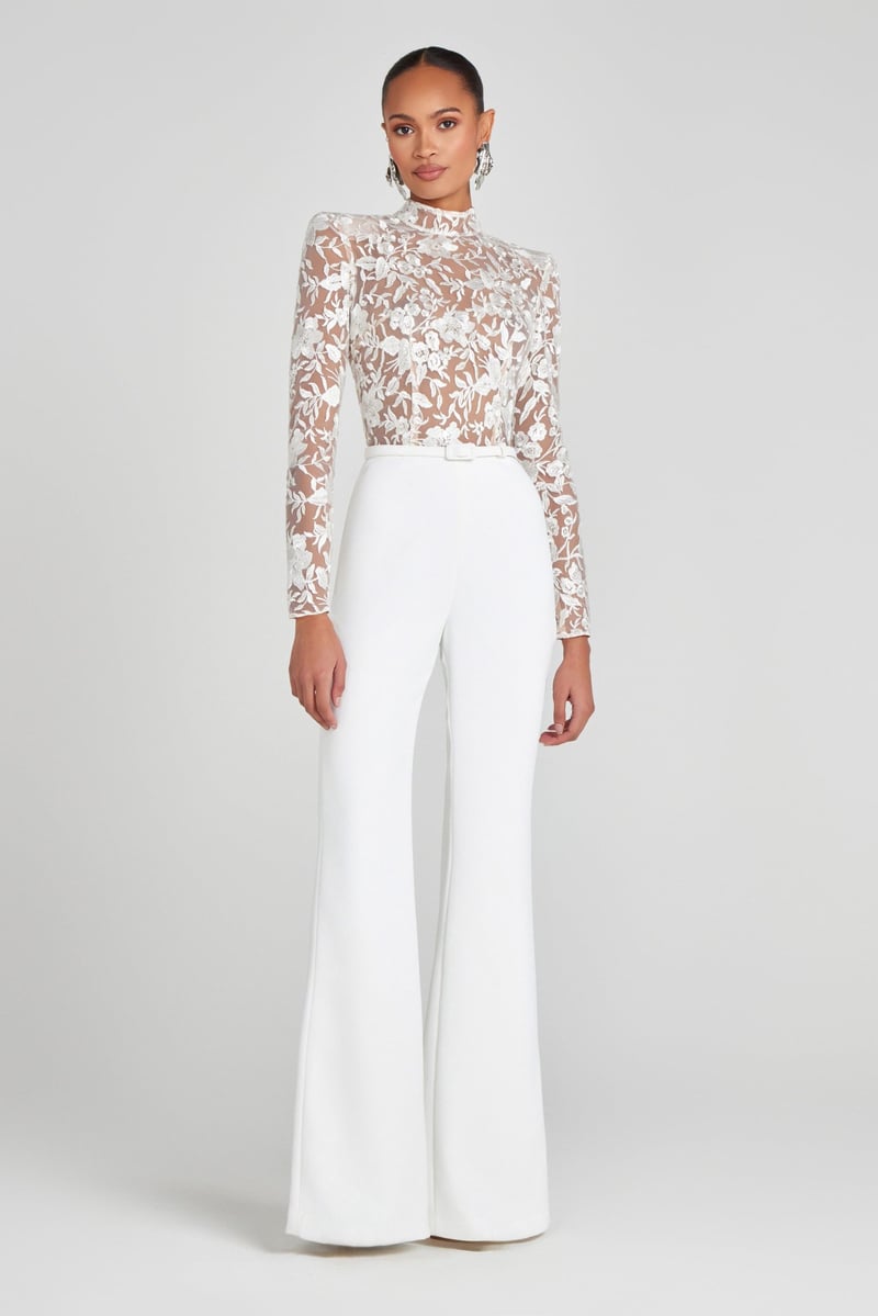 a model wears a white long sleeve wedding jumpsuit with high-neck lace bodice and flared trousers.