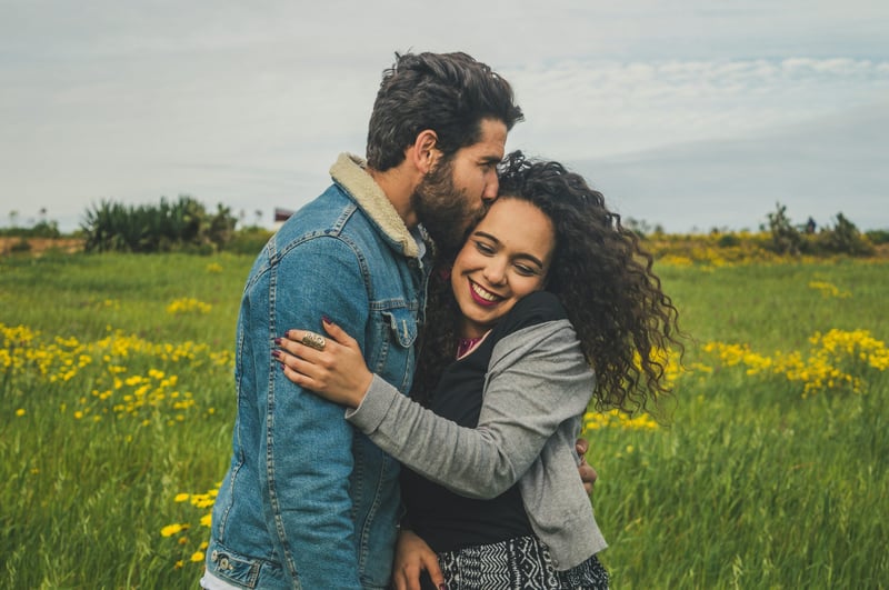 A man kissing a woman on the head as they pose together in a field
