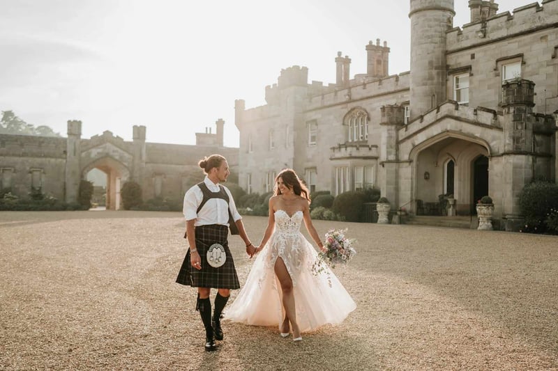 Groom in a kilt hand in hand with a bride walking outside of Dundas Castle