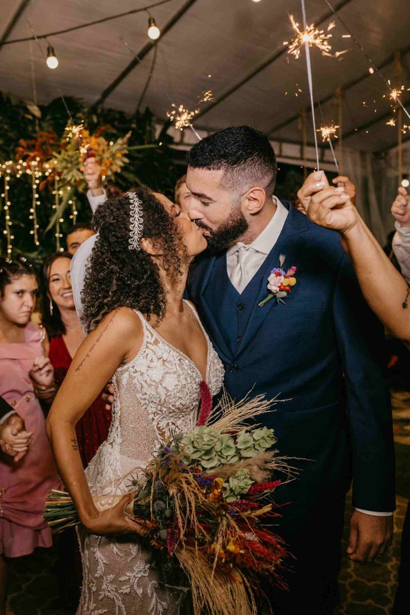 Bride and groom kissing at a boho, festival themed wedding as guests wave sparklers around them