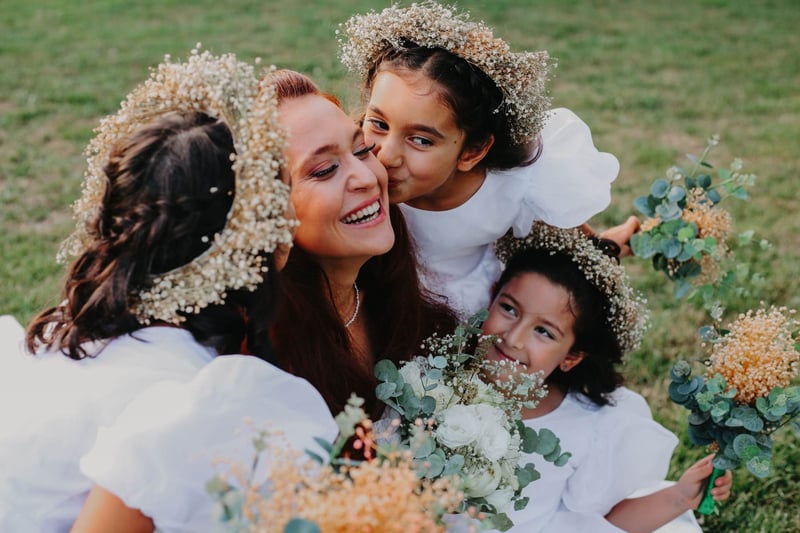 Three flower girls surrounding a bride and kissing her