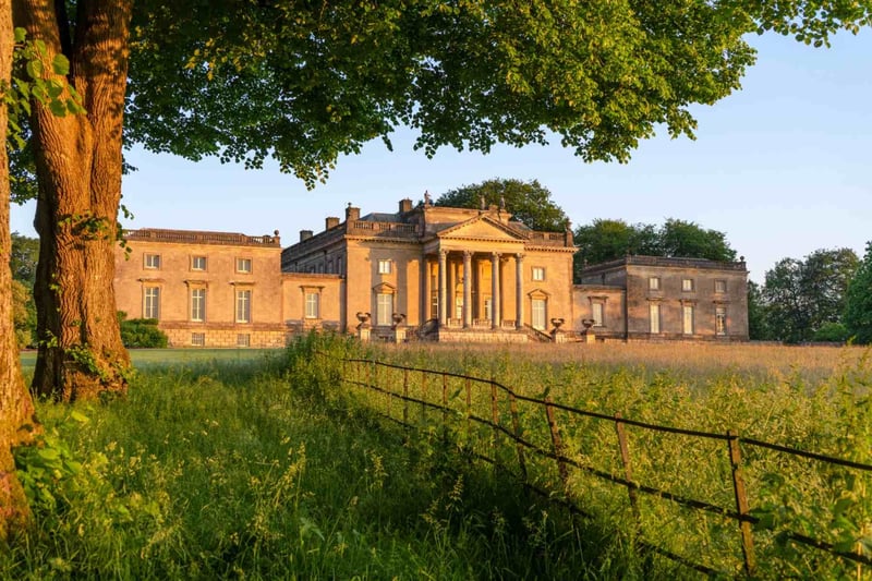 Golden hour exterior of a grand Palladian country house wedding venue with classical columns and wildflower meadow