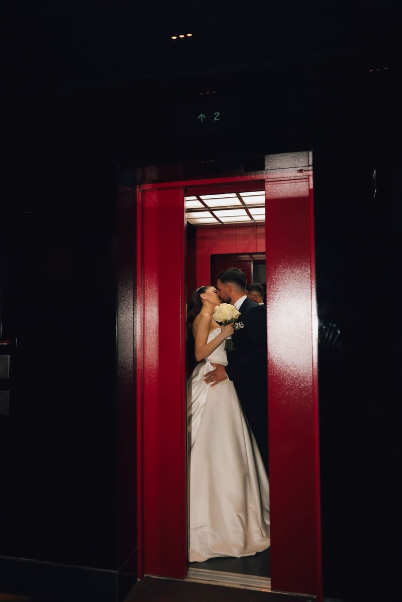 A newlywed couple shares a romantic kiss in a modern elevator setting