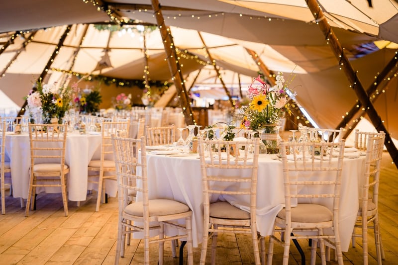 interior of a tipi wedding tent set up for an english country garden reception with white table linen and seasonal flowers.
