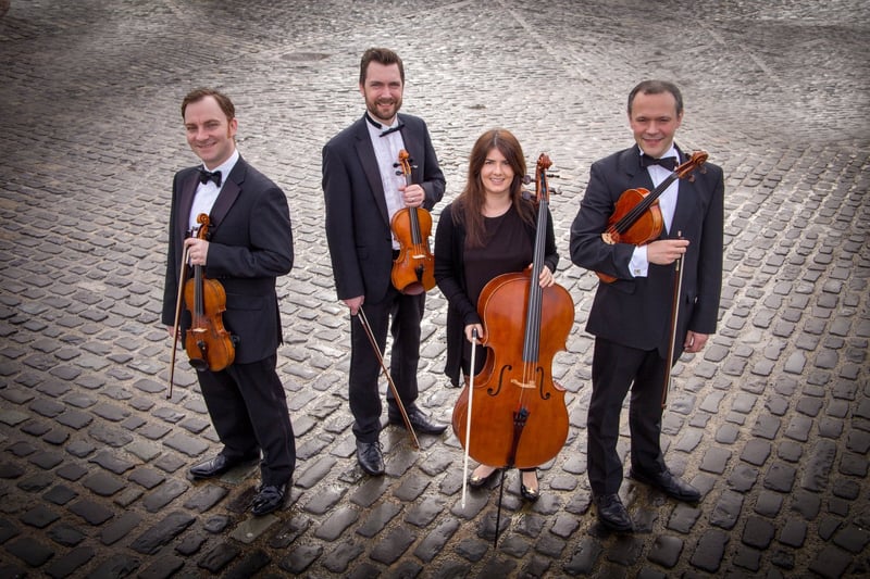 a group of four string musicians stand with their instruments while wearing black formalwear.