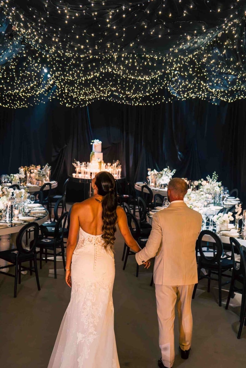 Rear view of a bride and groom walking hand in hand into a celestial themed wedding reception, looking up at the starlit ceiling