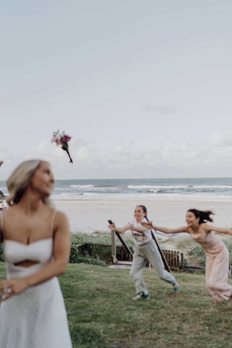 Bride throwing the bouquet as two wedding guests lunge for it
