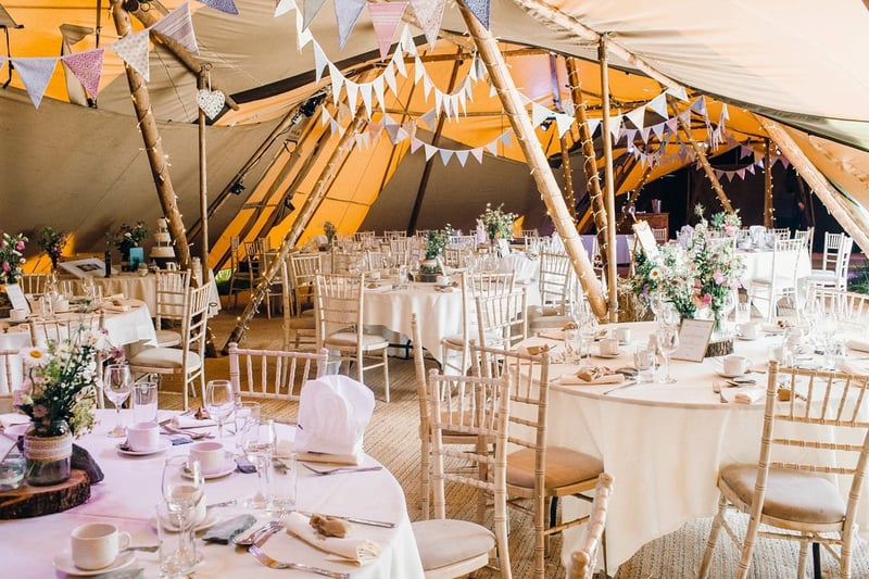 interior of a tipi wedding tent set up for a reception with pastel coloured bunting.