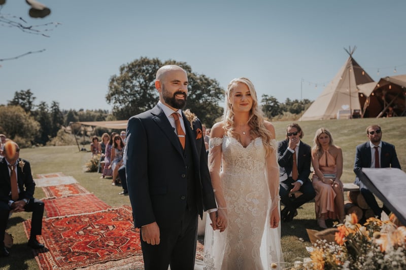 a bride and groom stand at the altar of their outdoor wedding with a tipi tent in the background.