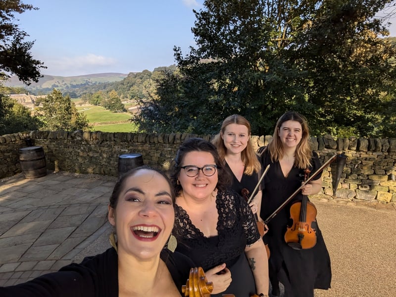 an ensemble of four female musicians smile as they take a selfie.