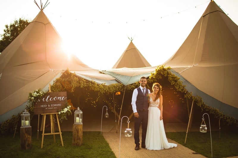 a bride and groom smile as they stand outside their tipi wedding venue in the peak district at golden hour.
