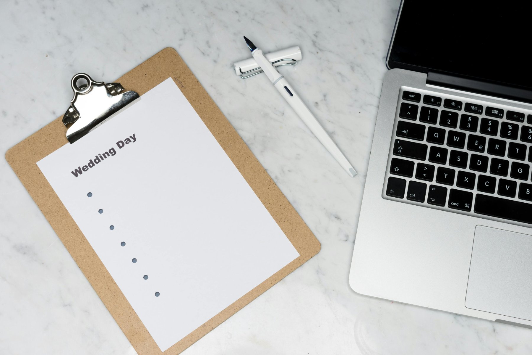 A laptop with a clipboard next to it and a piece of paper that says 'wedding day'