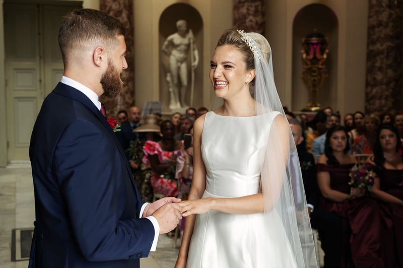 a bride grins as her groom places a ring on her finger during their wedding ceremony.