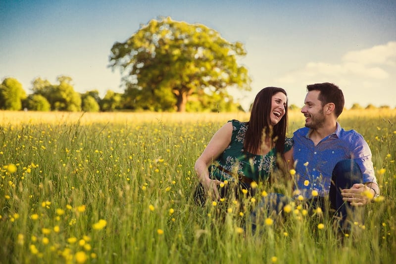 an engaged couple laughing in a field of yellow flowers.