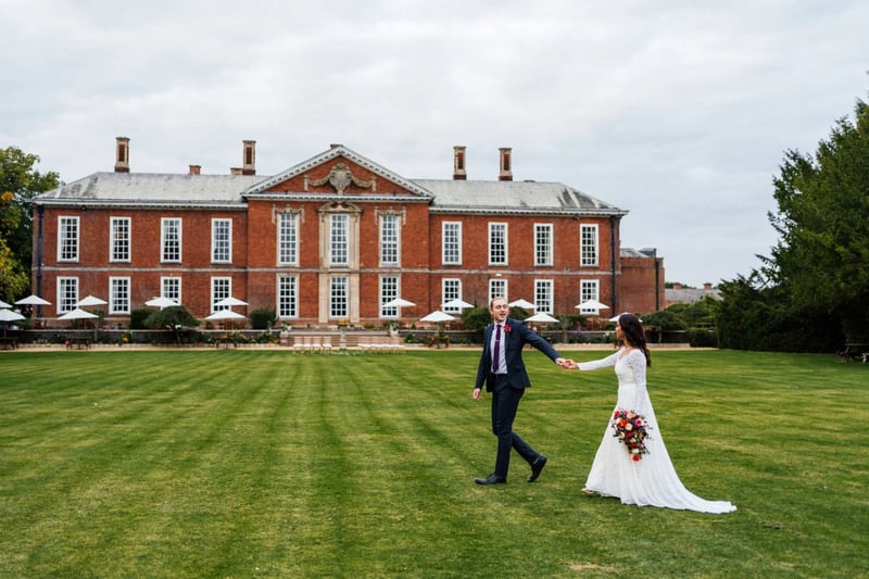 Bride and groom walking hand in hand on the lawn outside of a stately home wedding venue