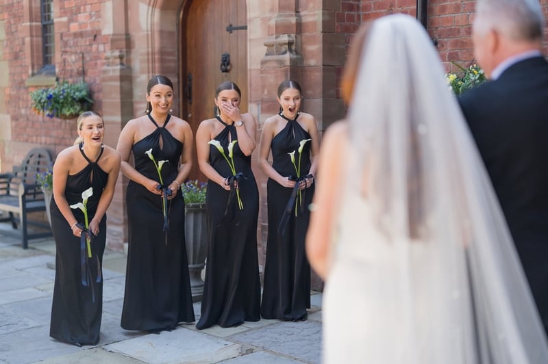 bridesmaids wearing black and holding a single calla lily gasp and smile as they see the bride for the first time.