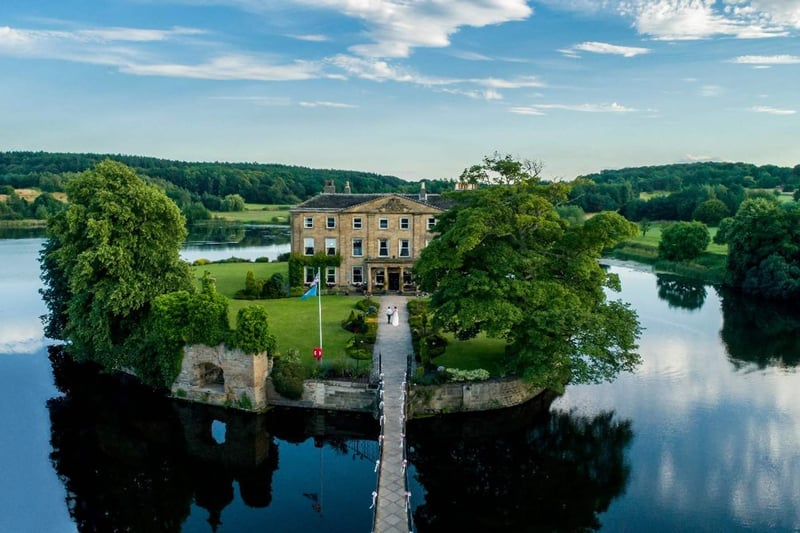 Aerial view of a stately home wedding venue on its own island surrounded by a lake, with a bridge leading to the venue