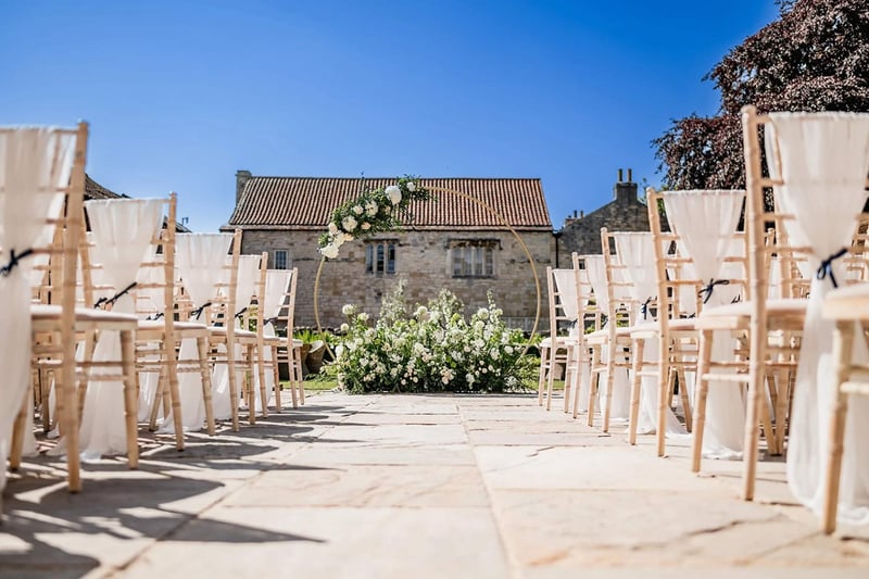 Outdoor wedding ceremony setup with Chiavari chairs and floral moon arch in a stone courtyard venue