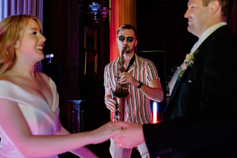 a wedding saxophonist plays as the bride and groom dance in the foreground.