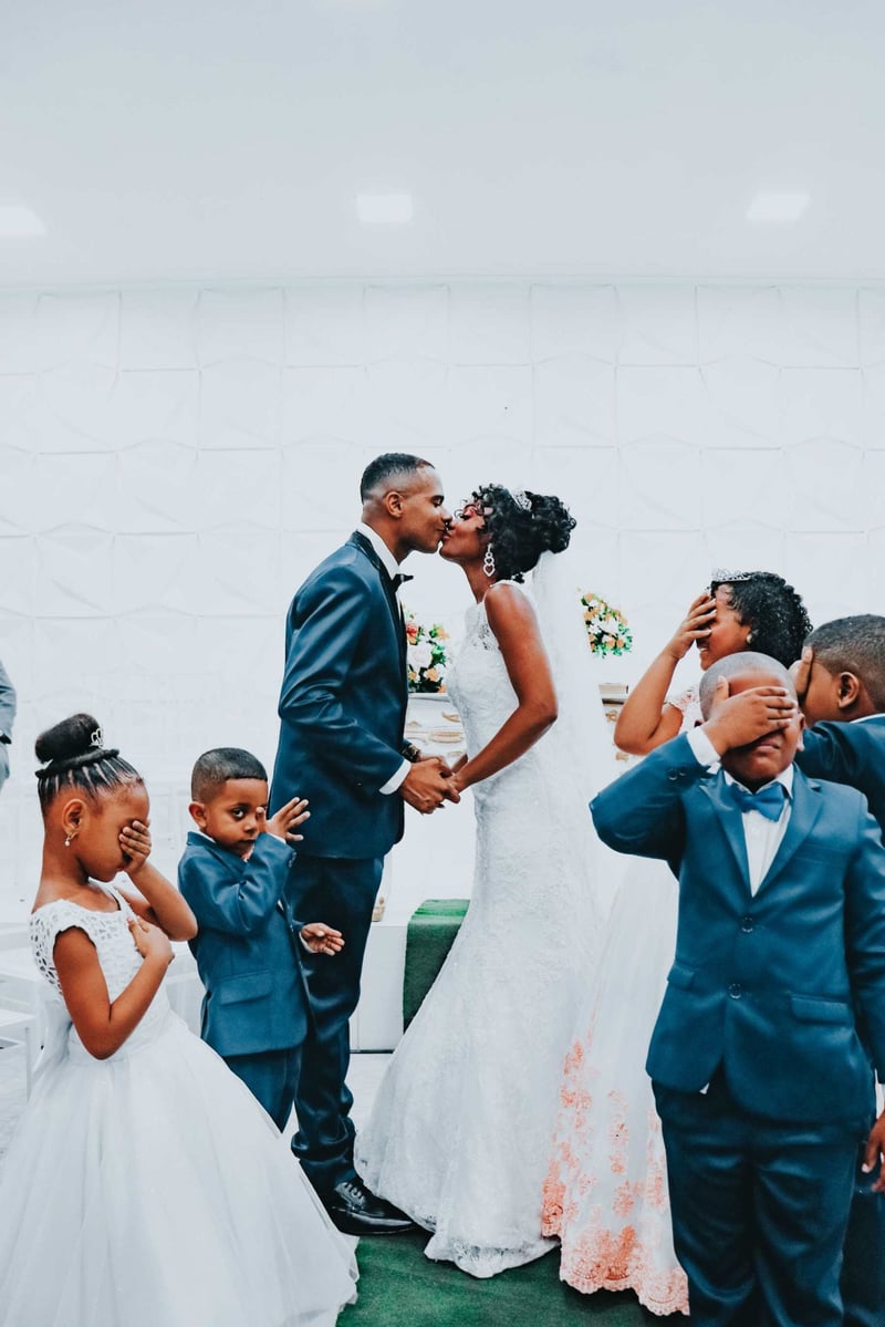 Bride and groom kissing as children surround them covering their eyes playfully