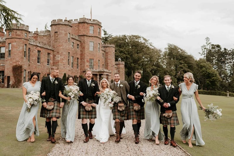 Bride and groom walking arm in arm with their wedding party in traditional scottish wedding attire outside a castle wedding venue in aberdeenshire