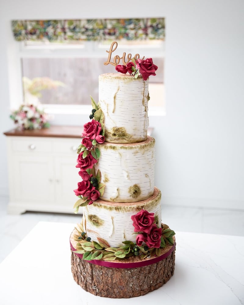 a rustic-style wedding three-tiered wedding cake with red flowers atop a log slice.