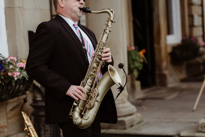a male saxophone player in a suit plays an acoustic set outdoors.