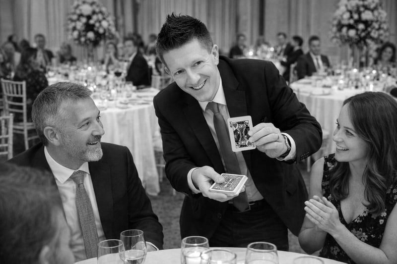 a magician holds up a card and smiles as his performs magic at a wedding breakfast.