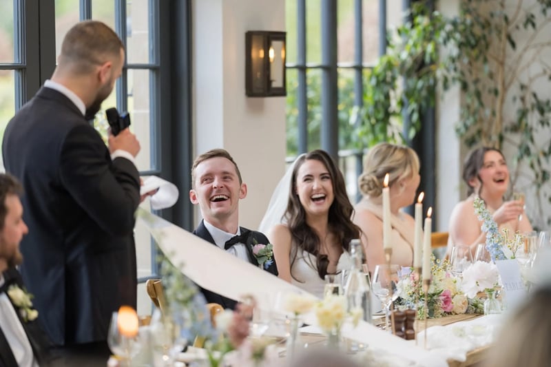 Bride and groom laughing as the best man gives his speech