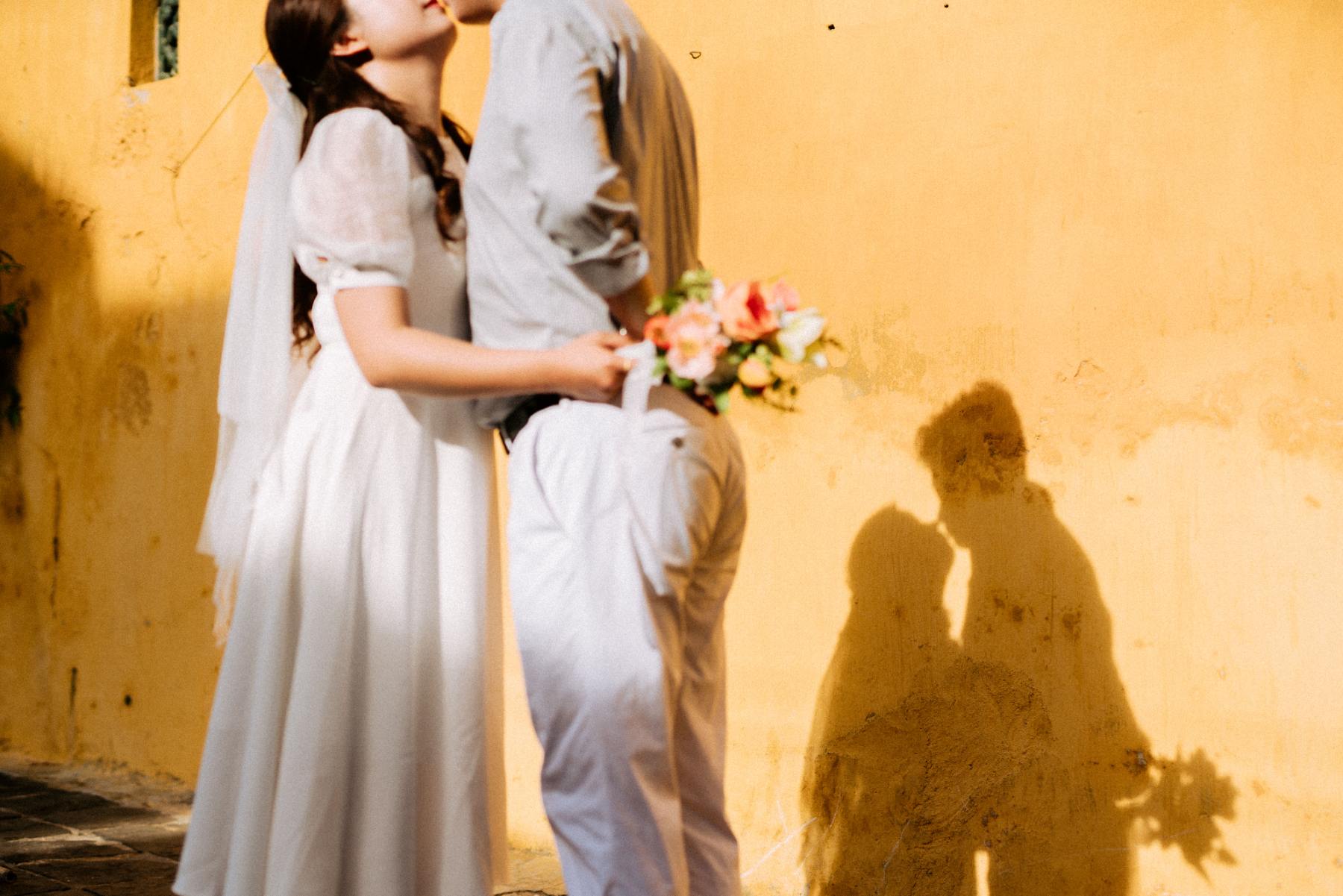 Bride and groom kissing in front of an orange wall with their shadows cast against the wall