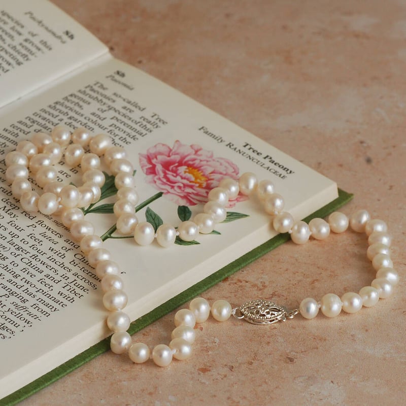 pearl necklace draped over an open book with a silver clasp