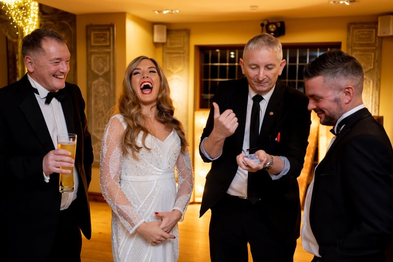 a magician performs a trick as a bride and two groomsmen laugh.