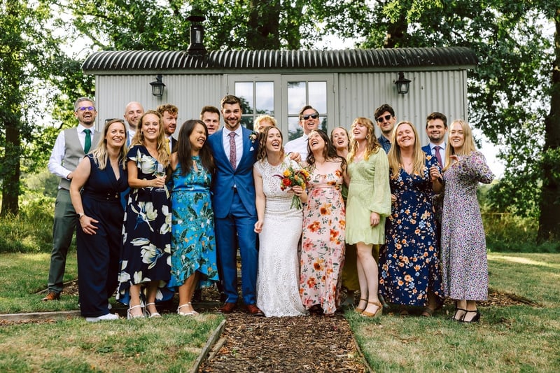 a relaxed group photo of a bride and groom and their guests who are wearing colourful outfits.