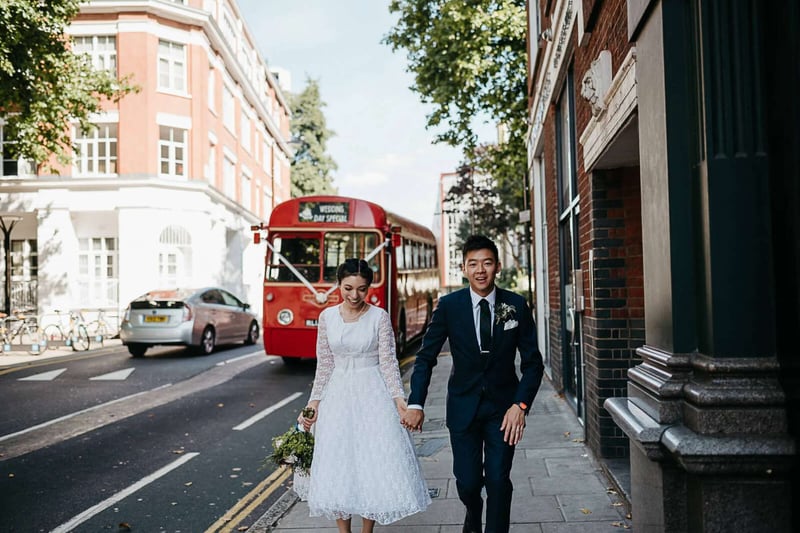 Bride and groom walking hand in hand at a london wedding with a red bus visible in the background