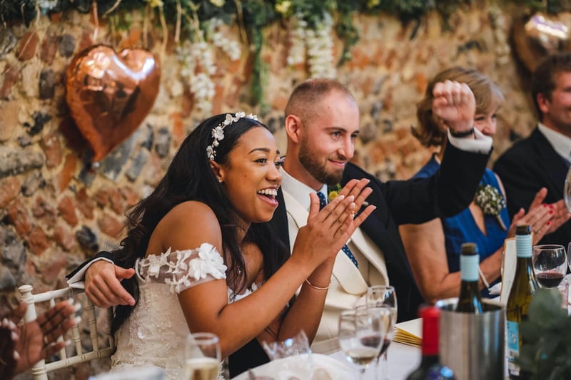 Bride laughing at a best man's speech as the groom cheers