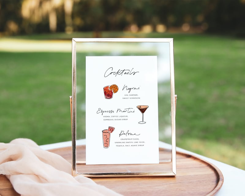 a wedding cocktail menu in a glass frame at an outdoor wedding.